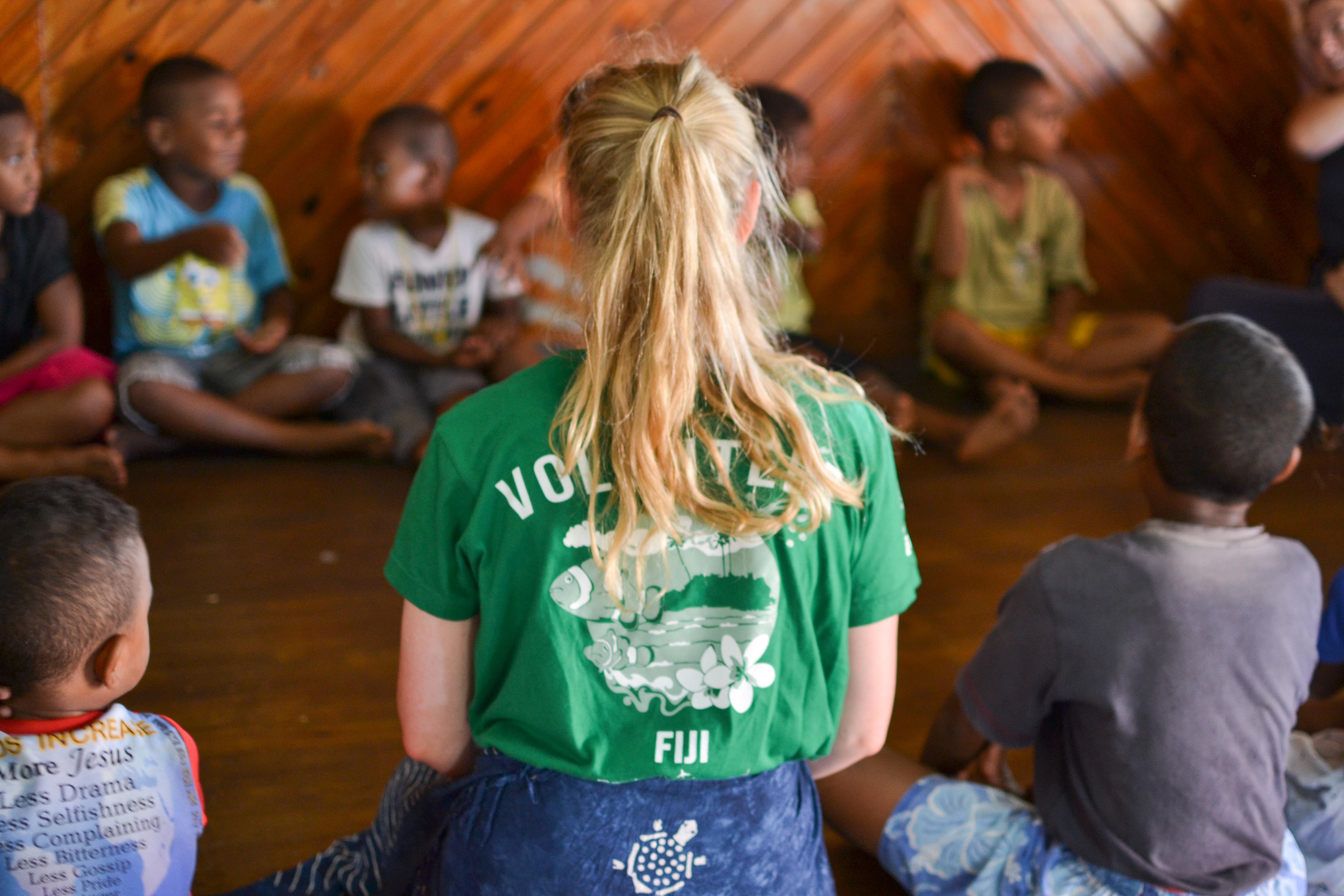Female Projects Abroad Community Volunteer sits with a group of children at a holiday program during Community volunteer work in Fiji. Female Culture and Community volunteer sits in a circle with school children in a Day Centre during a Community Project in Fiji.